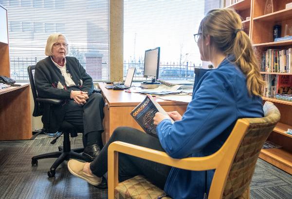 A student is seen from behind as she talks with a faculty member.