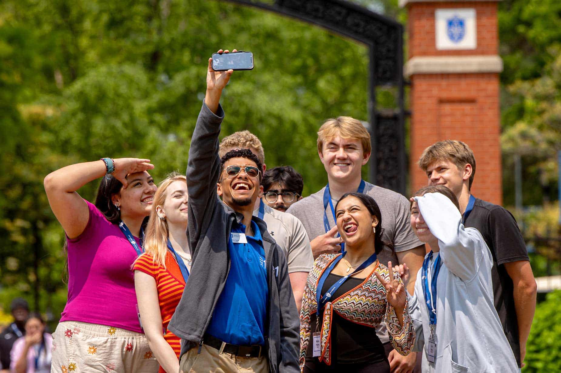 A male SLU 101 leader holds up his cell phone to take a selfie with a group of incoming students. Everyone is smiling or making funny faces at the camera.