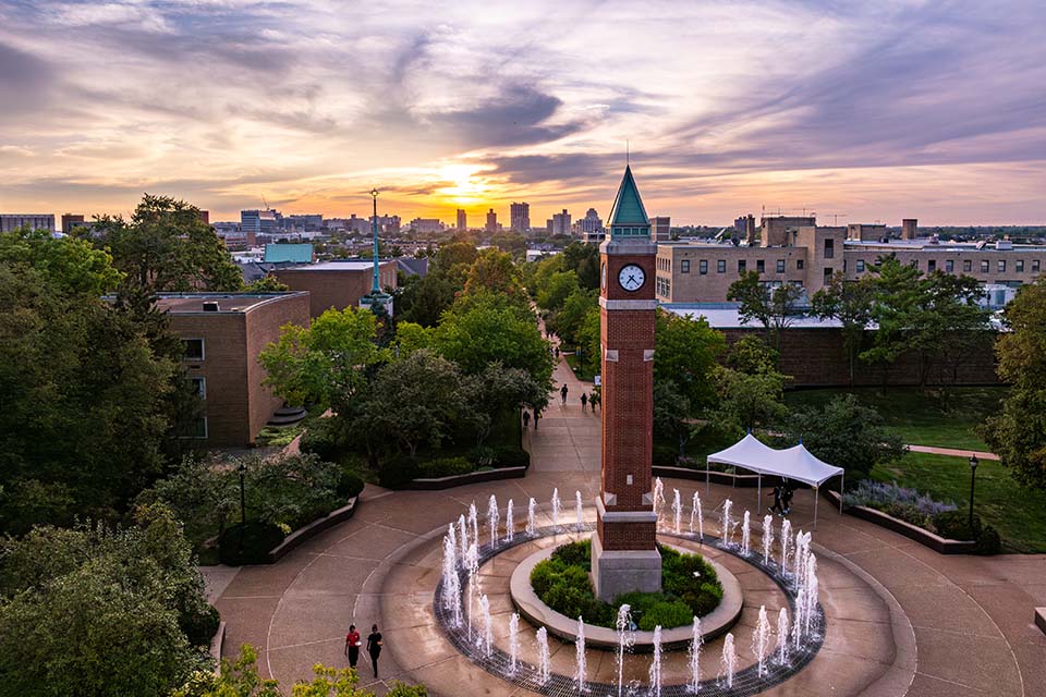 The clock tower on campus seen with a fountain surrounding it at sunset.