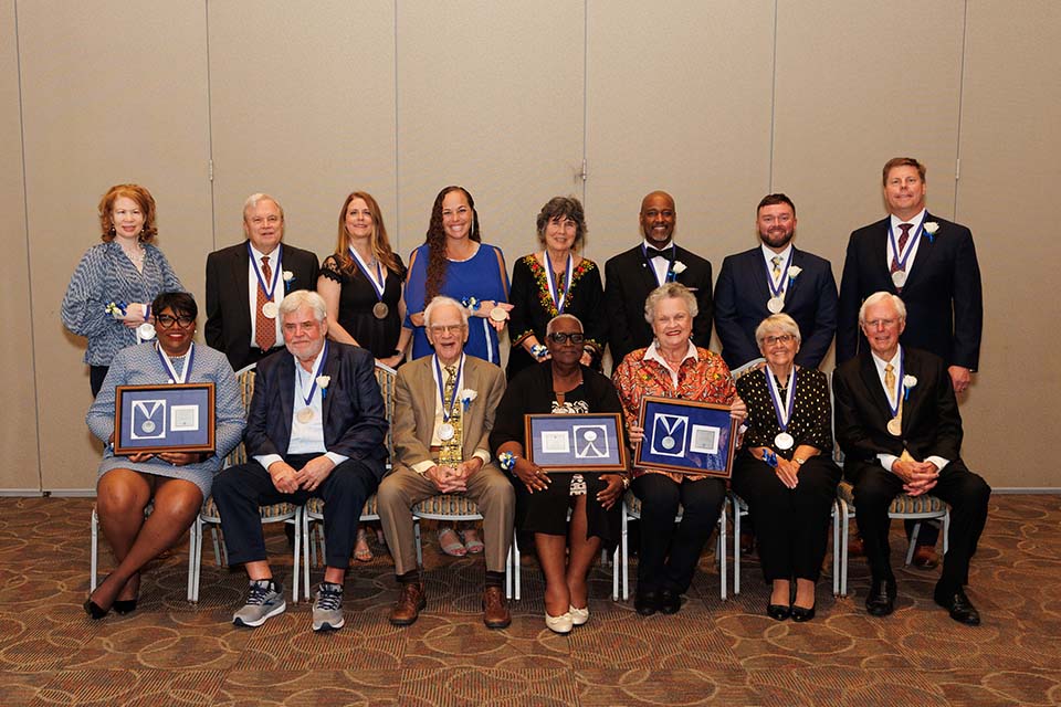 A group of men and women pose for a photo together, some holding framed medals.