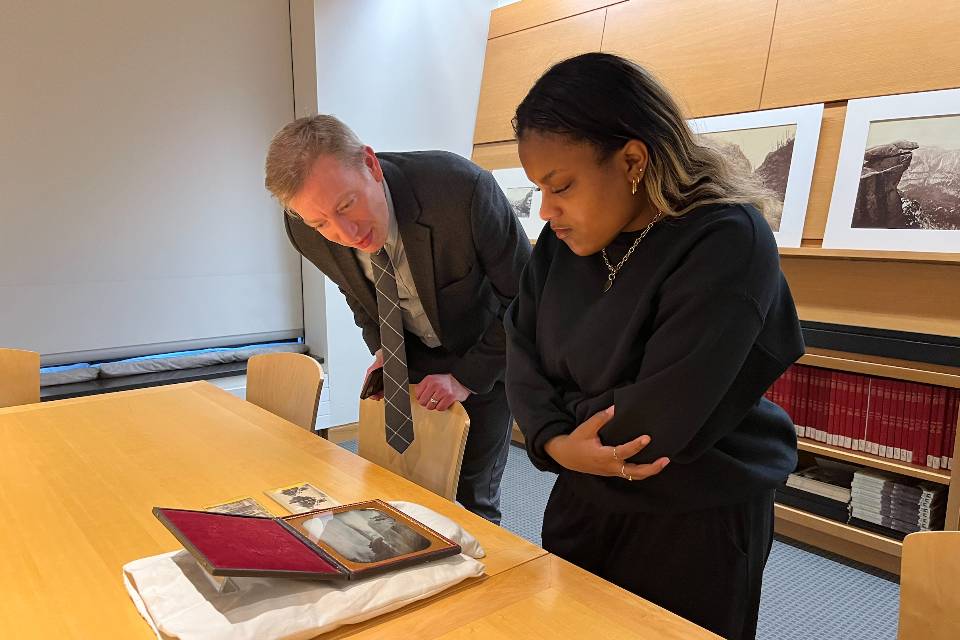 A student and professor examine an historical art piece on a library table.