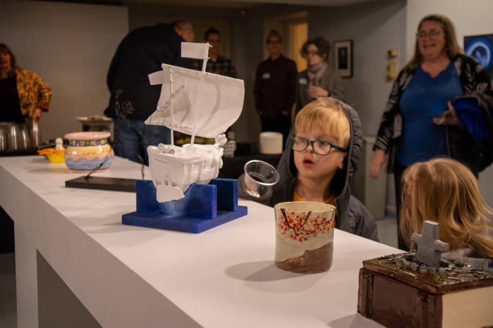 A young child examines a piece of pottery in a clear display case.