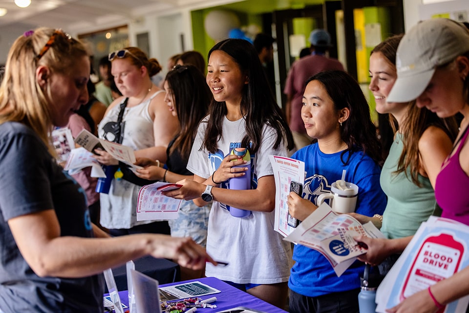 A group of students talk to a staff member at an information table.