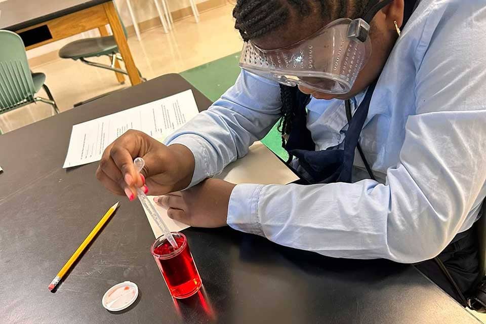 A young girl uses a pipette to get a red liquid out of a beaker. 