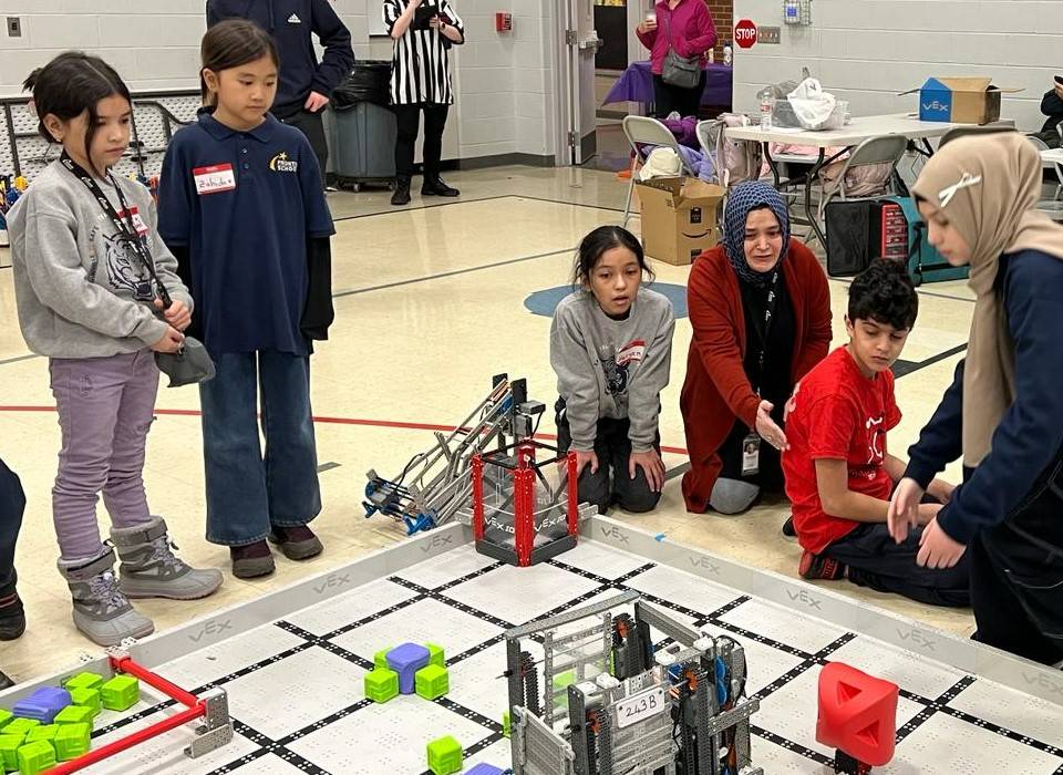 Frontier Schools students at Vex Robotics competition. Students and adults examine materials on a gym floor during a robotics competition.