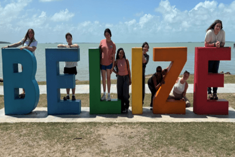 SLU students and faculty stand on a 3-D sign with letters that spell out Belize. A beach and ocean are visible in the background.