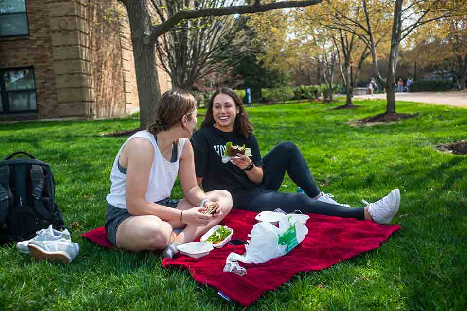 Two students eat on a blanket outside on SLU's campus.