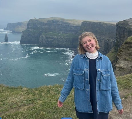 Addie is standing on a cliff overlook the sea.