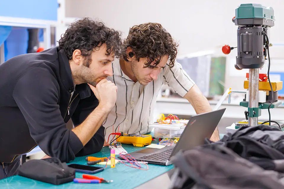 Teacher and student look at information on a laptop next to an engineering mechanical equipment.
