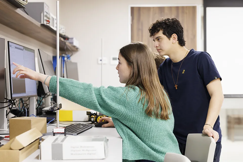 Science and Engineering at SLU-Madrid. Two students talk to a professor while looking at a laptop.