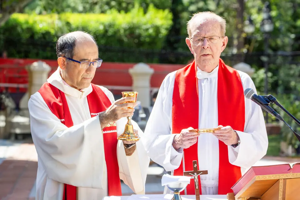 SLU-Madrid mass Two priests stand at an altar outside, while one holds a golden cup and another holds a golden plate.