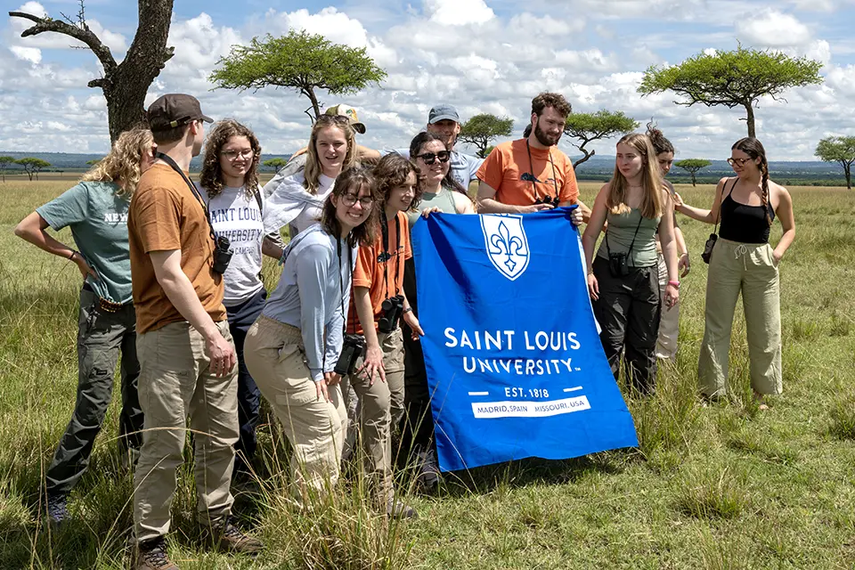 Landscape with a group of students in a grassy savanna, holding a SLU banner.