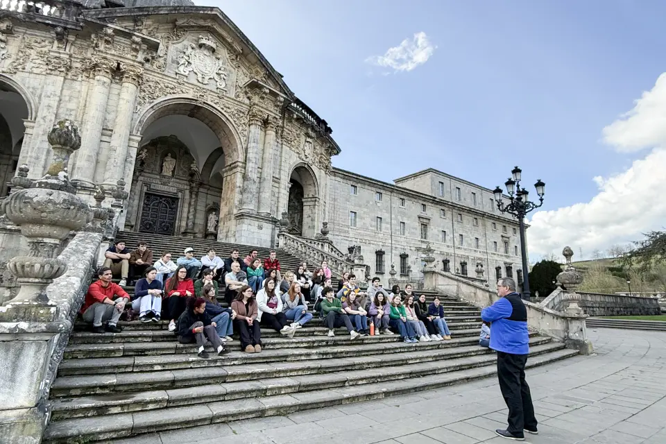A group of students sits on the steps outside of the Sanctuary of Loyola, a Baroque style building.