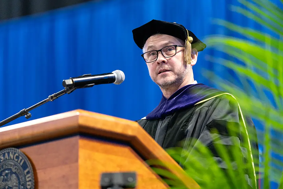 William Johnson on stage talking to the audience from a lectern with a microphone.