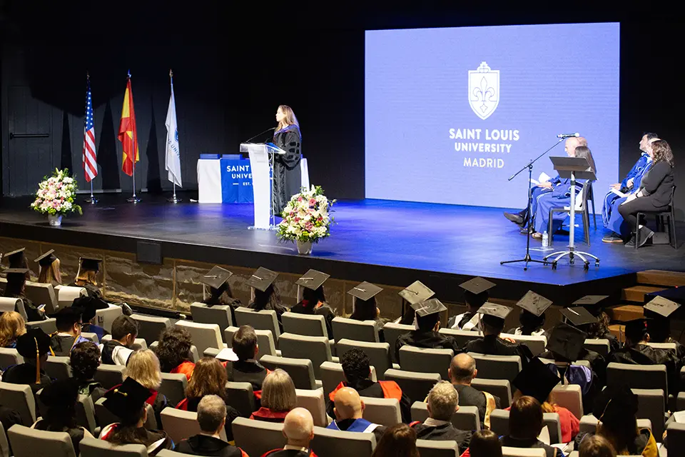 Woman talks at podium on stage in front of crowd in auditorium.