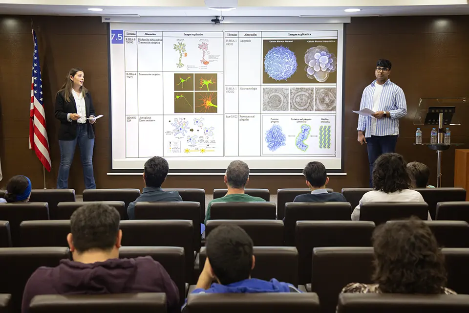 Two students present with a PowerPoint projected in the background in an auditorium.