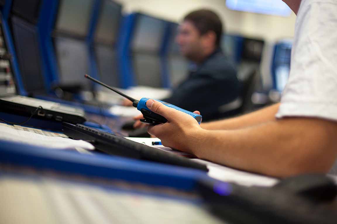 Emergency management A hand holding a walkee talkee at a desk with a computer with a man in the background