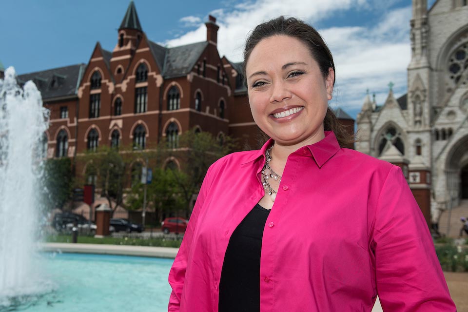A smiling student stands in front of the fountain across the street from DuBourg Hall and St. Francis Xavier College Church